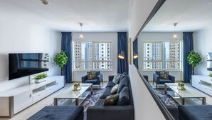 Een moderne woonkamer met een zithoek, een televisie en een grote spiegel die de kamer weerspiegelt.