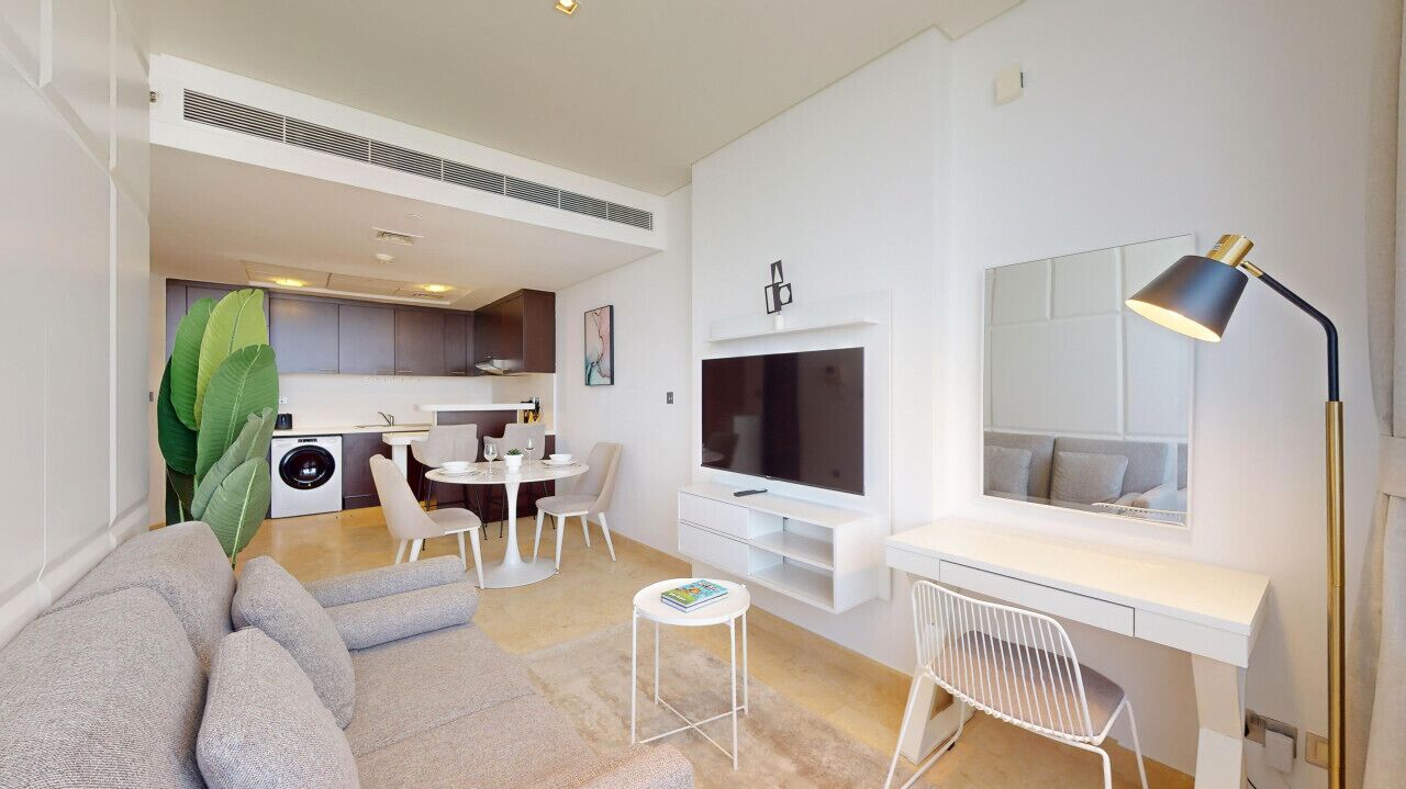 Una sala de estar moderna con sofá, comedor, televisor y escritorio con lámpara.
