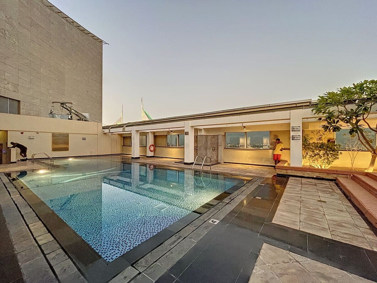 Ein Pool mit gefliestem Deck, einem Rettungsschwimmerstuhl und einem Gebäude mit Flachdach im Hintergrund.