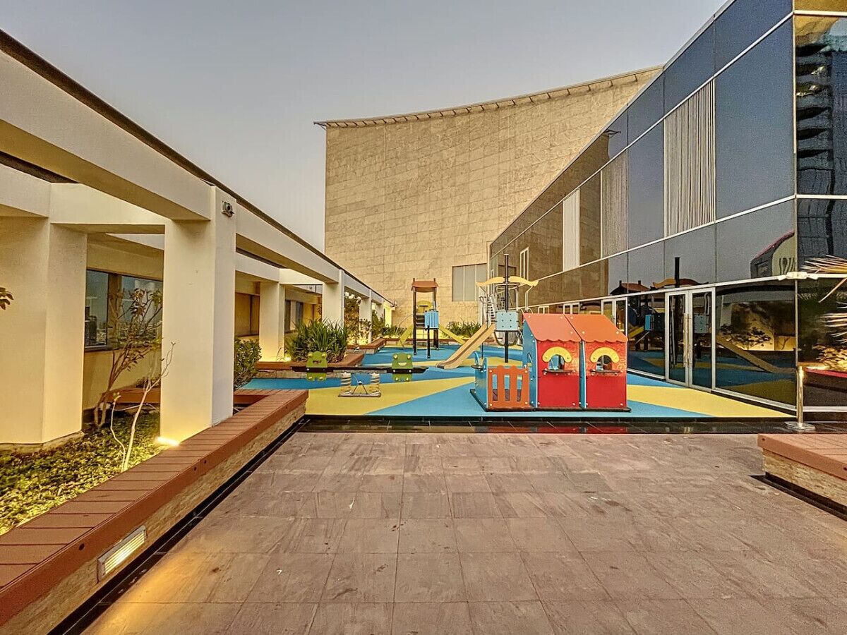 An outdoor area with a play structure, a small pool, and a building with a curved roof.