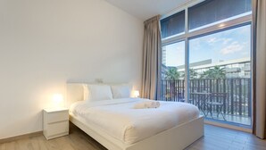 Une chambre d’hôtel avec un grand lit, deux tables de chevet avec des lampes et une vue sur un balcon aménagé avec du mobilier d’extérieur.