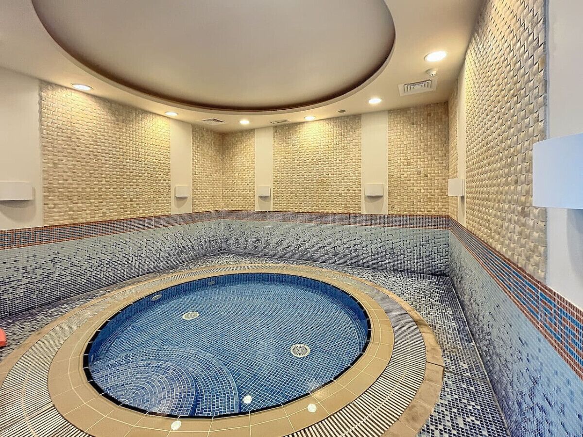 Une piscine intérieure de forme circulaire, bordée de mosaïques et dotée d’une fontaine centrale.