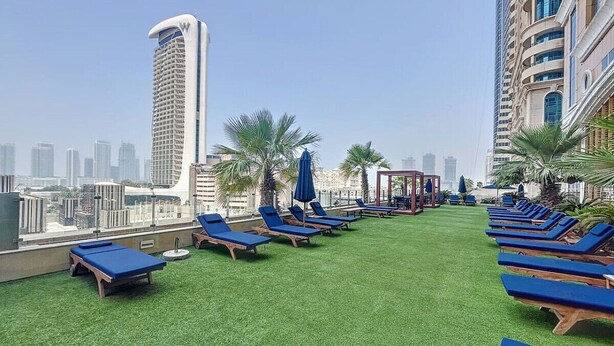 Um terraço com grama sintética, espreguiçadeiras e guarda-sóis, com vista para um horizonte urbano repleto de edifícios altos.