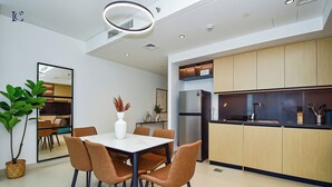 A modern kitchen with wooden cabinets, a stainless steel refrigerator, and a dining area with a white table and brown chairs. - 2bedroom Apt in Burj Crown (Dubai)