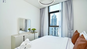 A hotel room with a large bed, a bedside table with a mirror, and a view of a cityscape through a window. - 2bedroom Apt in Burj Crown (Dubai)