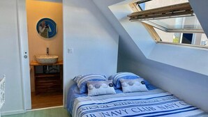 A bedroom with a skylight, a bed with navy-themed bedding, a circular mirror, and a wooden vanity. - VILLA KEROMER GÎTE DE LO (ETEL)