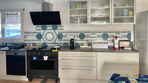 A modern kitchen with a dishwasher, oven, and microwave. There are cabinets with glass doors above the counter, and a television mounted on the wall. - VILLA KEROMER GÎTE DE LO (ETEL)
