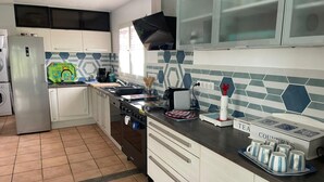 A modern kitchen with white cabinets, a stainless steel refrigerator, a stove, and a sink. There are various kitchen items on the counter, including a kettle, a coffee maker, and a tray of cups. - VILLA KEROMER GÎTE DE LO (ETEL)