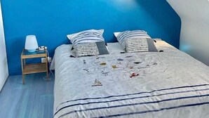 A bedroom with a sloped ceiling, a bed with striped bedding, two bedside tables with lamps, and a painting on the wall. - VILLA KEROMER GÎTE DE LO (ETEL)