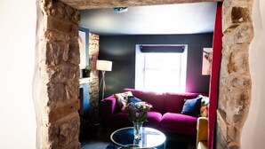 A cozy living room with a stone archway, a pink sofa, a glass coffee table, and a window with curtains. - Wave Cottage Bristol (Bristol)