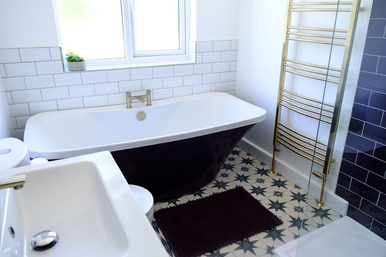 A bathroom with a freestanding bathtub, a white sink, and a window with a plant.