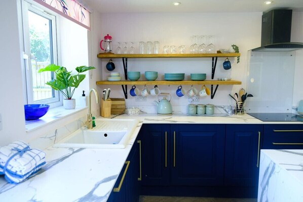 A modern kitchen with dark blue cabinets, a white countertop, and a window with a plant.