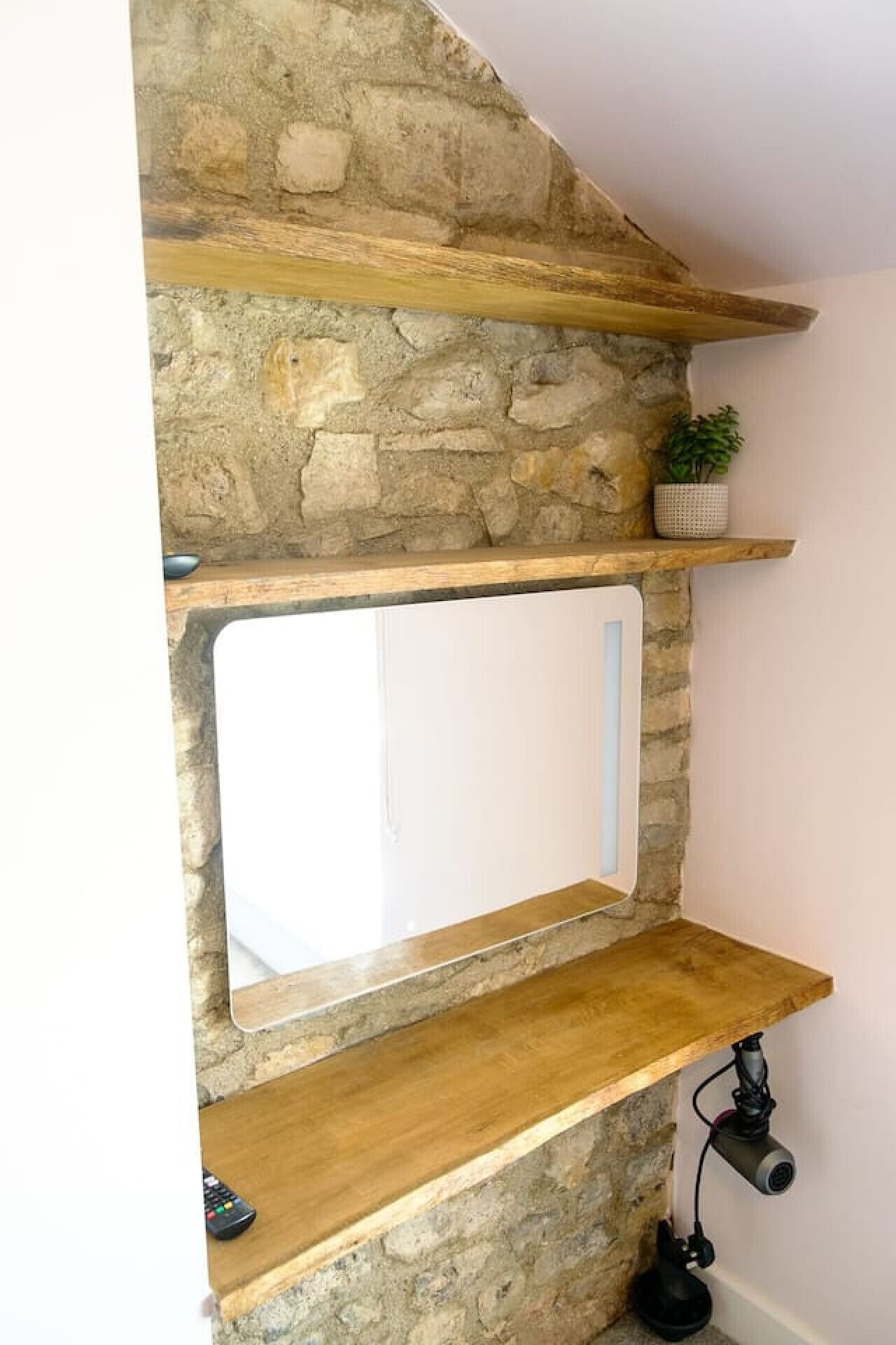 A stone wall with wooden shelves and a mirror.