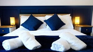 A neatly made bed with white linens and two dark blue pillows, flanked by two bedside lamps. - Wave Cottage Bristol (Bristol)