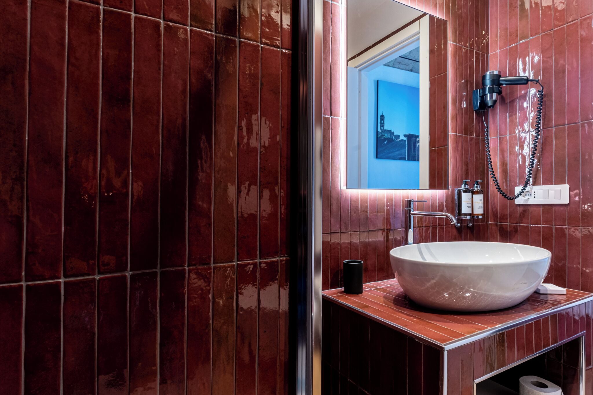 A bathroom with a large white sink, a handheld showerhead, and a mirror reflecting a cityscape.