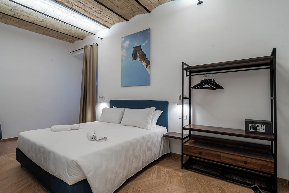 A bedroom with a bed, a wooden bench, a radio, and a painting on the wall.