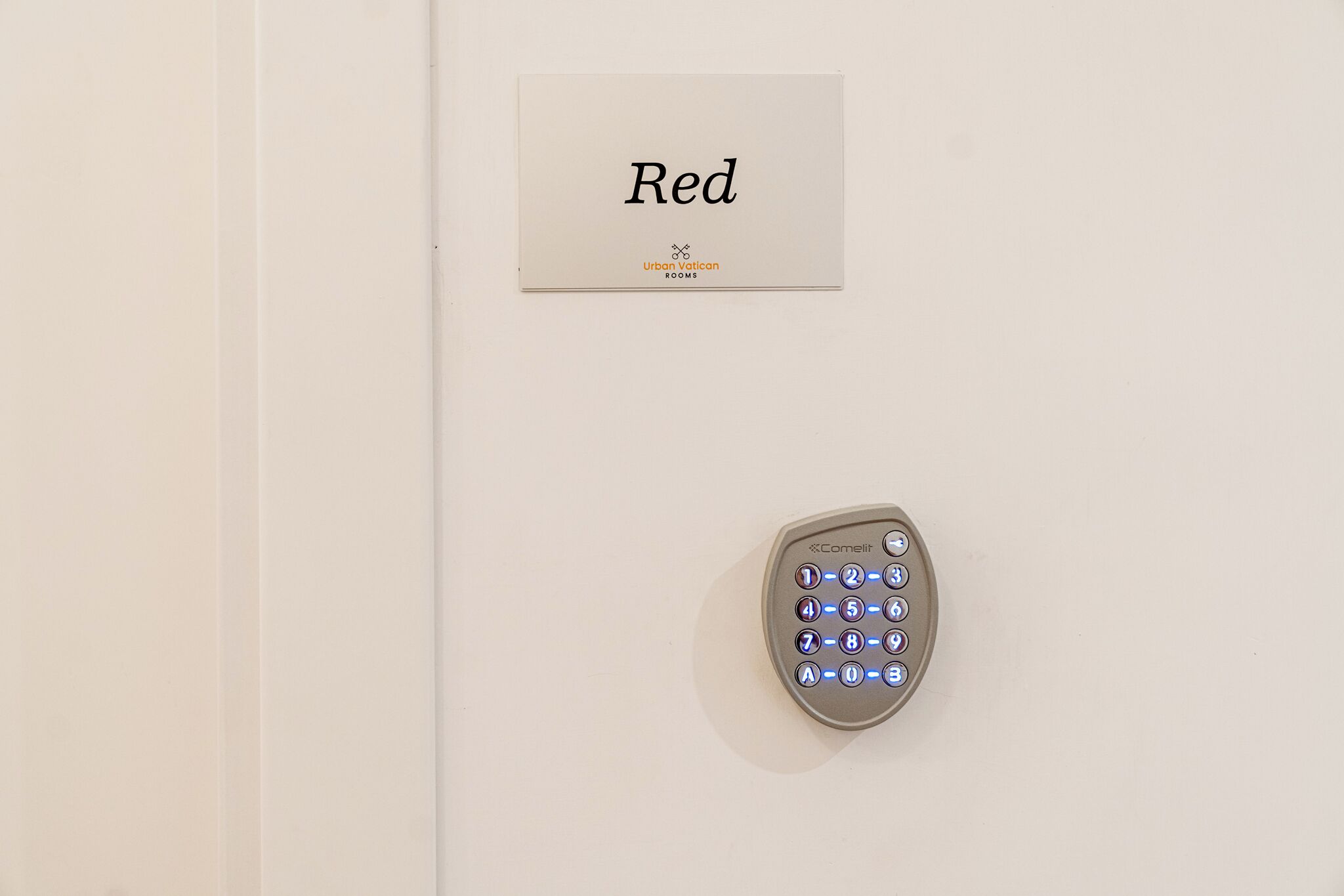 Un interphone fixé au mur et une enseigne indiquant « Red Urban Vatican Rooms ».