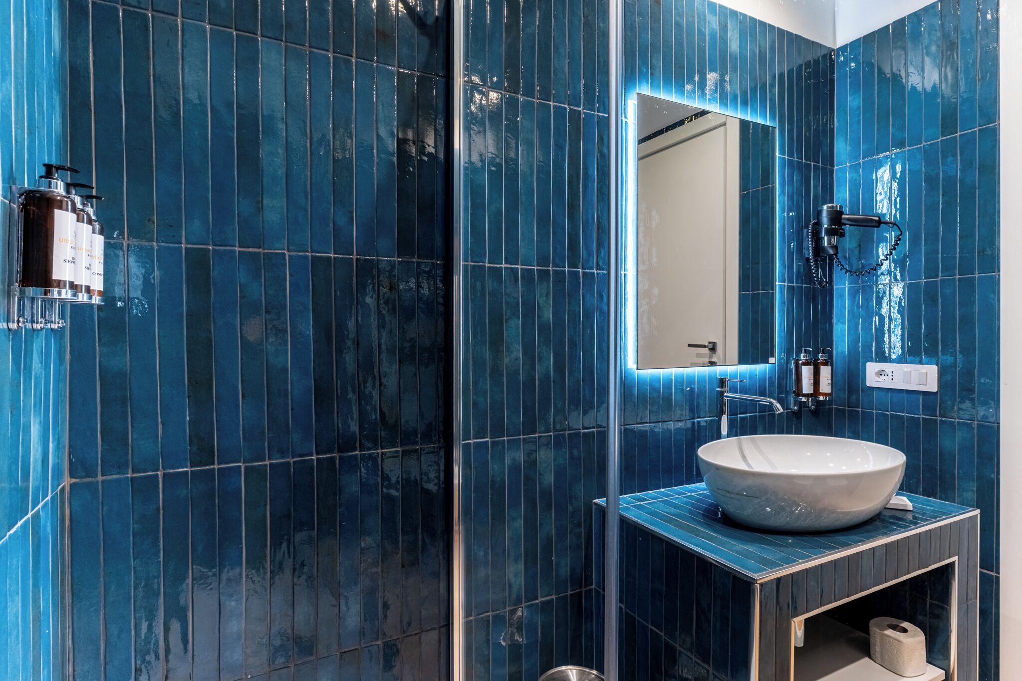 A bathroom with blue tiles, a white sink, and a mirror.