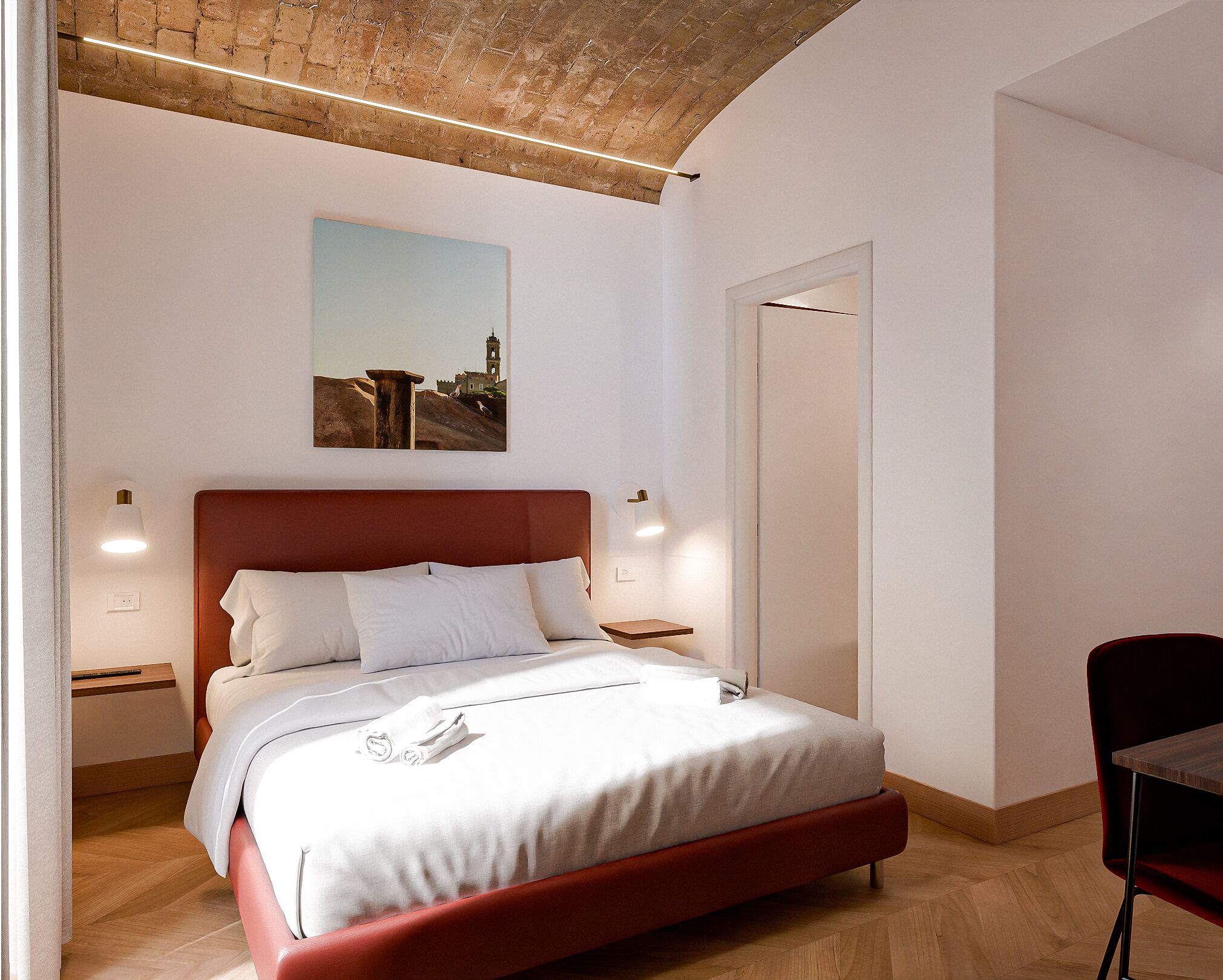 Un dormitorio moderno con cabecera roja, cama individual con ropa blanca, mesita de noche con lámpara y un cuadro con vista a la ciudad en la pared.