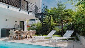 A modern outdoor pool area with lounge chairs, a dining set, and a spiral staircase leading to an upper level. - Villa with private heated pool by the sea in Royan (Royan)