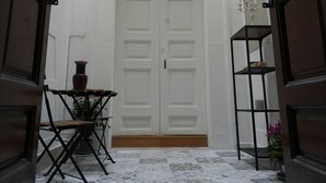 A narrow hallway with a white door, a small table with a vase, and a shelf with a potted plant.