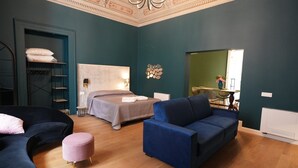 A modern bedroom with a bed, two sofas, a small round ottoman, and a wardrobe.