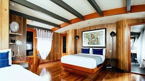 Ein Schlafzimmer mit Holzboden, einem Bett mit weißer Matratze und blauen Kissen, einem Nachttisch, einer Lampe und einem gerahmten Bild an der Wand.