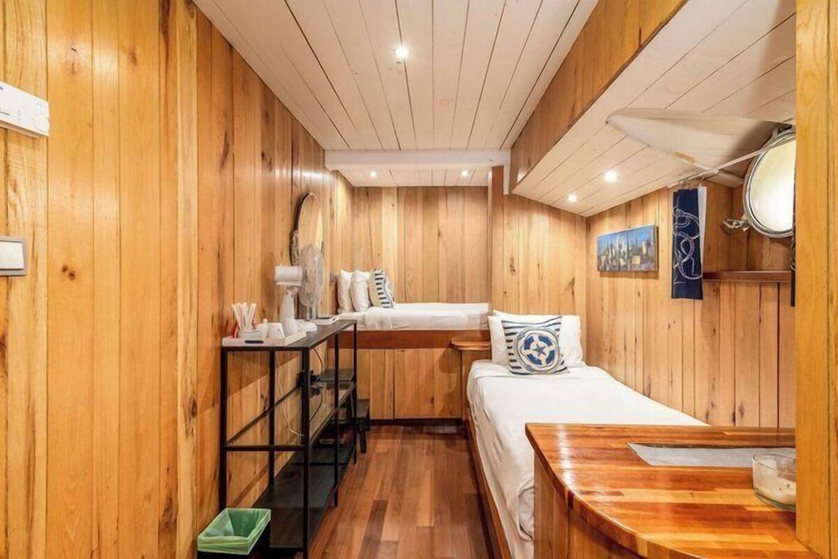 Una habitación de madera con una cama, una mesita, un banco y un calentador fijado a la pared.