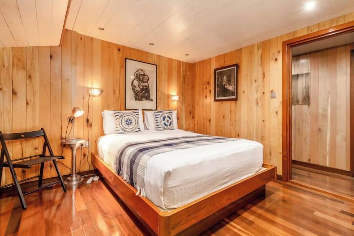 Un dormitorio con paneles de madera, una cama, dos lámparas fijadas a la pared y un cuadro enmarcado.