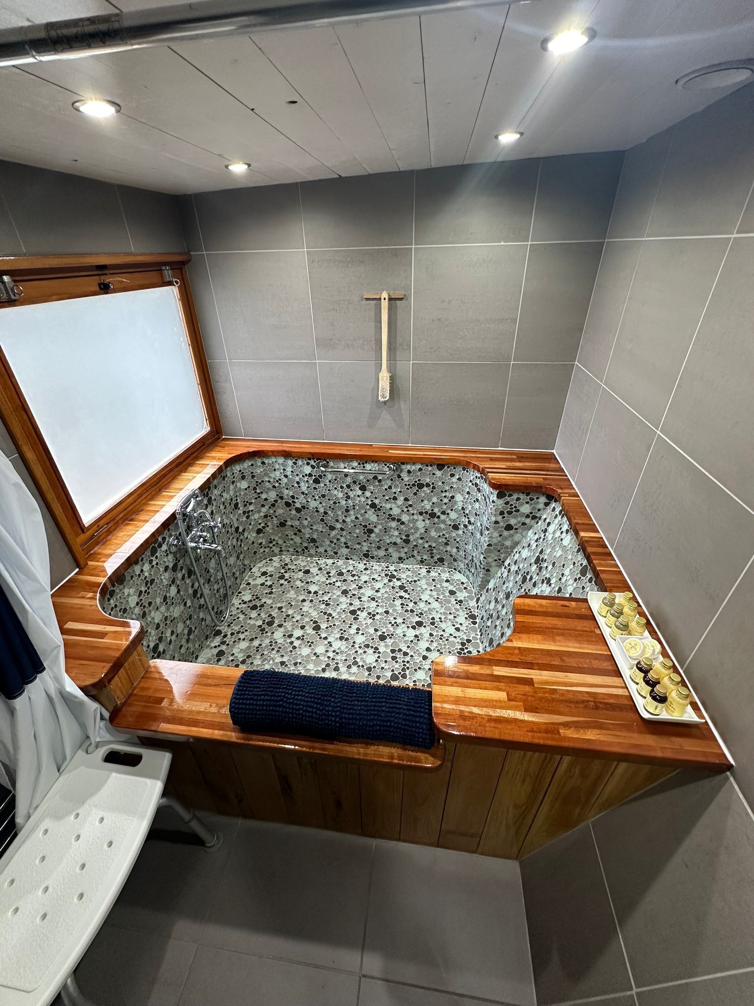 A modern bathroom with a freestanding bathtub, a wooden bench, and a shower area.