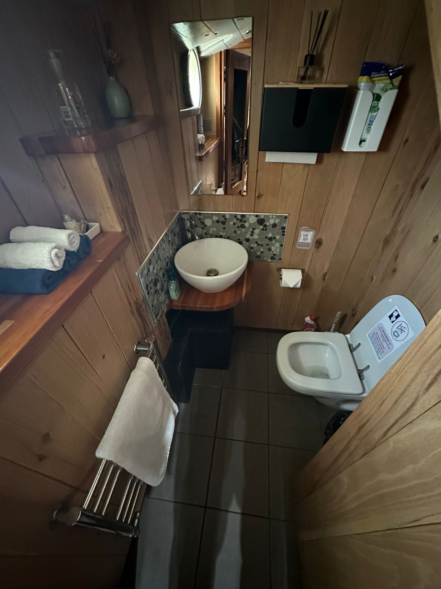 Une petite salle de bain au décor intérieur en bois, comprenant un lavabo, des toilettes et un miroir.