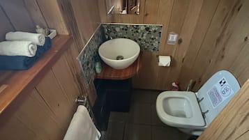 Une petite salle de bain au décor intérieur en bois, comprenant un lavabo, des toilettes et un miroir.