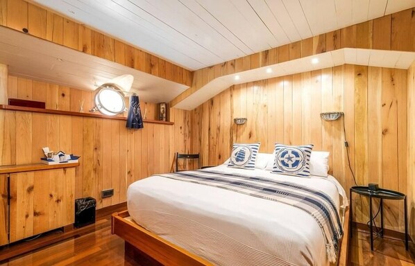 A wooden-paneled room with a bed, bedside table, and a small round mirror. - Le Sorelle (London)