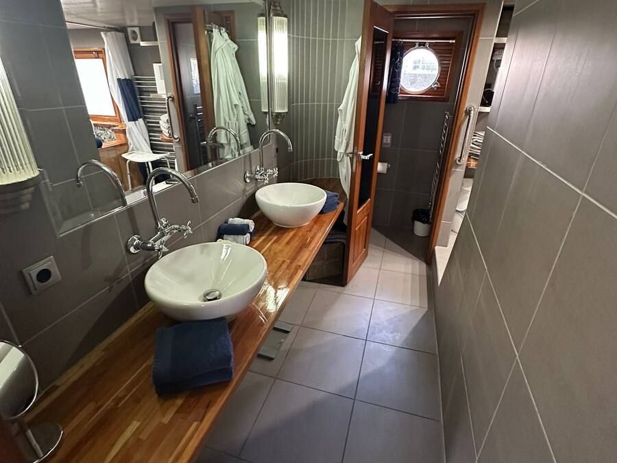 A modern bathroom with two sinks, a wooden vanity, a mirror, and a shower area.