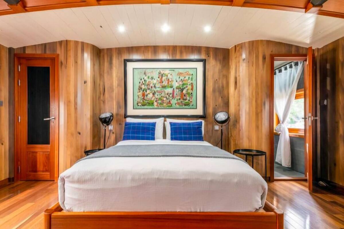 Un dormitorio con pared de paneles de madera, cama con ropa de cama blanca, una obra de arte enmarcada sobre la cama y una puerta a la izquierda.