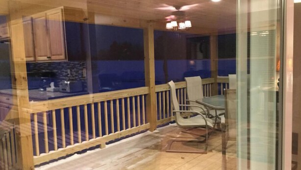 A covered outdoor area with a wooden deck, a glass enclosure, and a dining table with chairs. - The Tug Hill Lodge (Lyons Falls)