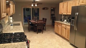 A kitchen with granite countertops, wooden cabinets, a stainless steel refrigerator, and a dining area with a table and chairs. - The Tug Hill Lodge (Lyons Falls)