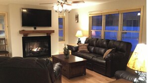 A living room with a fireplace, a television, a leather sofa, and a ceiling fan. - The Tug Hill Lodge (Lyons Falls)