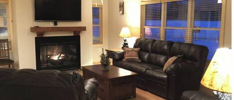 A living room with a fireplace, a television, a leather sofa, and a ceiling fan.