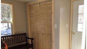 A room with a wooden bench, a sliding wooden closet, and a door with a doormat. - The Tug Hill Lodge (Lyons Falls)