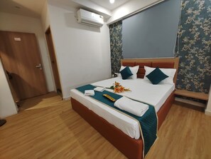 A neatly made bed with a teal bedspread, white linens, and decorative pillows. - Hotel Prasang (Surat)