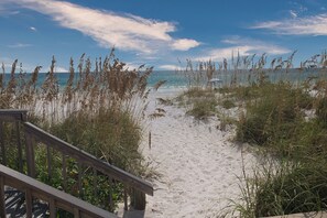 Un sentier de plage sablonneux, bordé d’herbes hautes et doté d’une rambarde en bois.