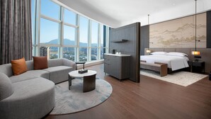 A modern hotel room with a large window, a sofa, a bed, a desk, and a view of the cityscape. - Wyndham Huaihua South (Huaihua)
