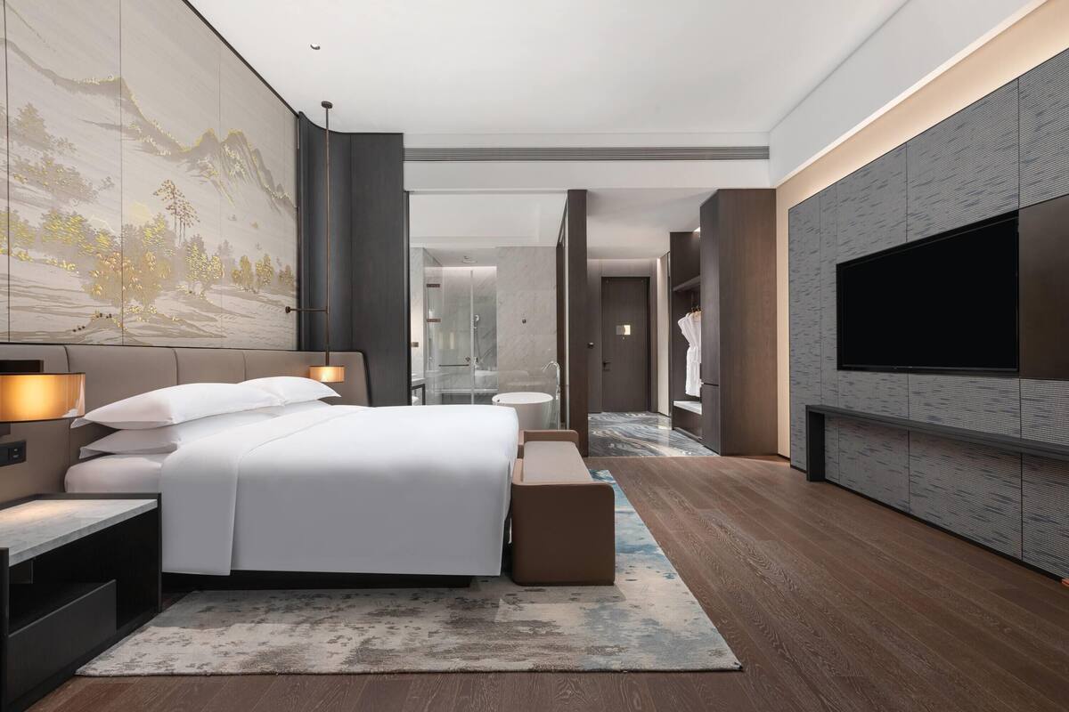 Ein modernes Hotelzimmer mit einem großen Bett, Nachttischen, einem Flachbildfernseher und einer großen Wandmalerei.
