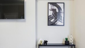 A modern living room with a flat-screen TV, a black abstract painting, and a black console table with decorative items. - Stylish 2BR Flat | Westcliff Seafront Stay (Westcliff-on-Sea)
