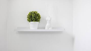 A white shelf with a potted plant and a white vase with reed sticks.