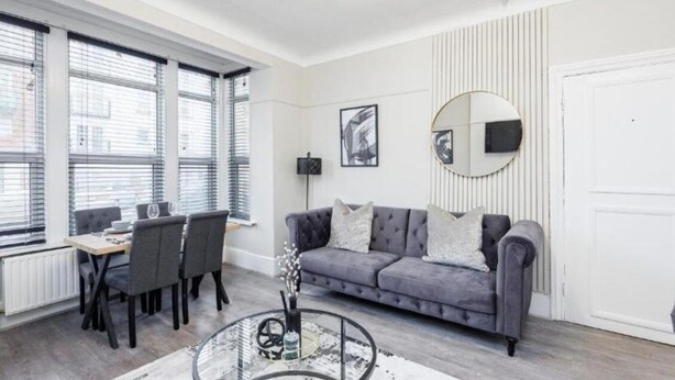 A modern living room with a grey sofa, a round coffee table, and a dining area with a table and chairs. - Stylish 2BR Flat | Westcliff Seafront Stay (Westcliff-on-Sea)
