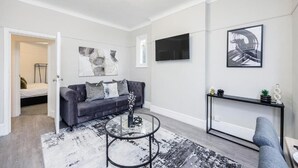 A modern living room with a grey sofa, a round coffee table, and a black console table with decorative items. - Stylish 2BR Flat | Westcliff Seafront Stay (Westcliff-on-Sea)