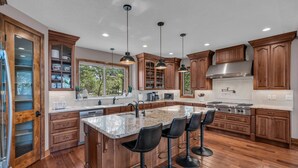 A spacious kitchen with wooden cabinets, a large island with bar stools, and a stainless steel range hood.