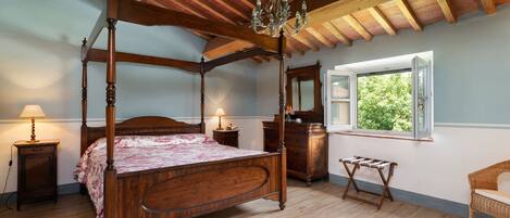 A four-poster bed with a wooden headboard, a chandelier, and a window with a view of greenery.